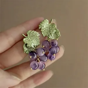 Close-up of grape-shaped earrings with purple beads and green textured leaves
