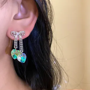 Detailed view of silver bow earrings with iridescent heart-shaped crystal tassels.