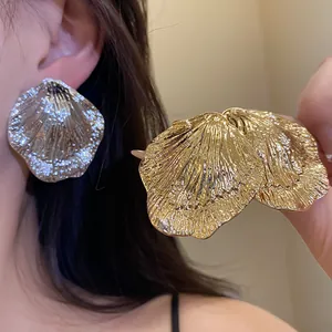 Close-up of large metallic leaf earrings with gold and silver textured finishes.