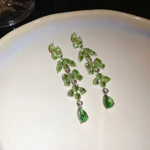 Close-up of elegant green leaf-shaped chandelier earrings on a ceramic plate