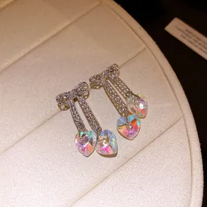 Close-up of iridescent heart drop earrings with bowknot crystal accents