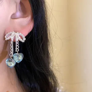Close-up of shiny bow stud earrings with blue heart-shaped crystal tassels.