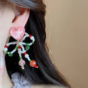 Detailed close-up view of pink heart and colorful beaded bow clip-on earring on a model ear