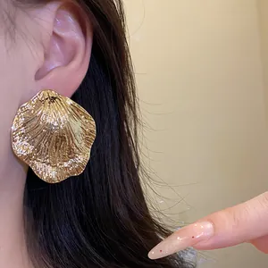 Macro detail view of a golden wrinkled leaf-shaped metal stud earring worn on a model ear.