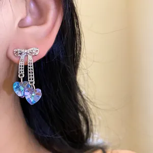 Close-up of iridescent heart tassel earrings with silver bow design on model's ear