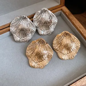 Close-up of oversized metallic wrinkled leaf stud earrings in elegant gold and silver tones