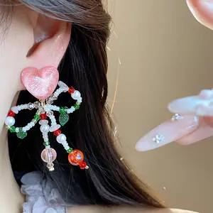 Close-up view of sweet beaded bow earrings with pink heart detail worn by model