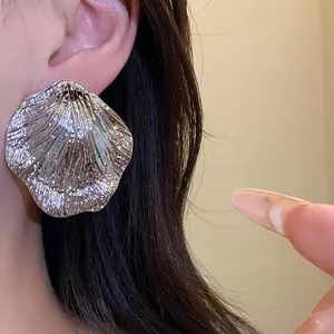 Macro view of a textured silver metallic leaf-shaped stud earring worn on an ear