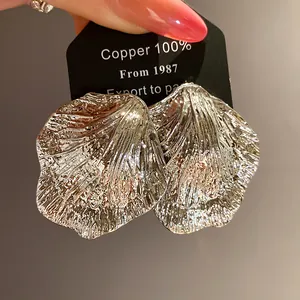 Macro detail of silver metallic wrinkled leaf earrings on a black display card