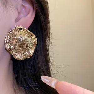 Close-up of large gold wrinkled leaf earrings on ear showing texture and metallic glow.