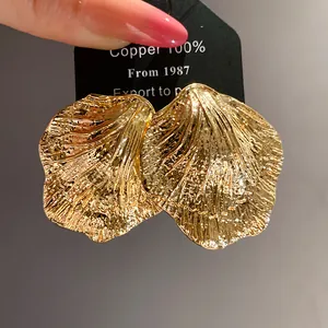 Detailed close-up view of golden textured crinkled metal leaf-shaped stud earrings on card
