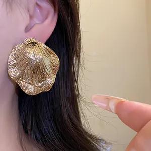 Detail view of large gold pleated leaf earrings showing metallic texture and shine.