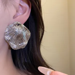 Close-up of metallic crumpled leaf stud earring worn on ear, showing silver-tone finish