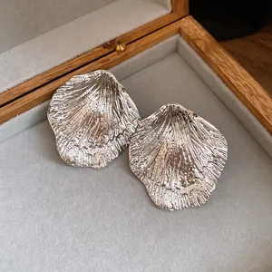 Detailed close-up of silver shell-shaped metallic stud earrings in a wooden jewelry box