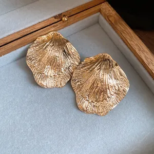 Detailed macro view of golden metal leaf stud earrings with unique wrinkled texture