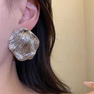 Detail view of a large silver wrinkled leaf earring worn on a model's ear