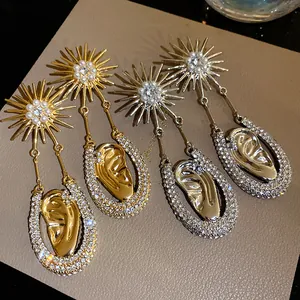 Dettaglio orecchini sole oro e argento con perle e motivo a forma di orecchio.