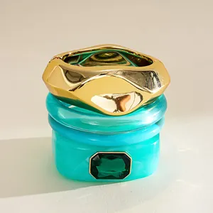 Gros plan d'un ensemble de bracelets en résine avec strass vert émeraude et jonc doré.