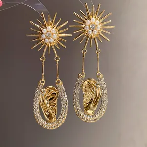 Dettaglio di orecchini a sole dorati con perle e pendenti a forma di orecchio con strass.