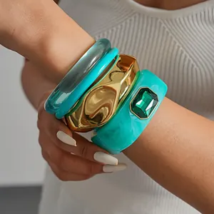 Gros plan de bracelets géométriques empilés en résine turquoise et métal doré sur un poignet