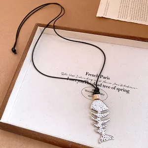 Detailed view of the hammered silver fishbone pendant on a black cord necklace.