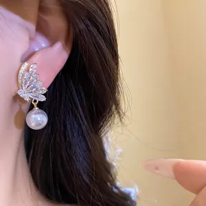 Close-up of elegant butterfly pearl earrings with sparkling zircon on a model's ear