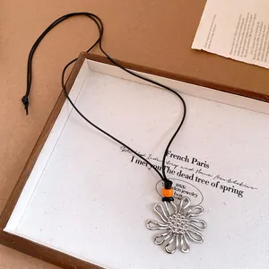 Close-up of a silver flower pendant necklace with an orange bead on a black cord