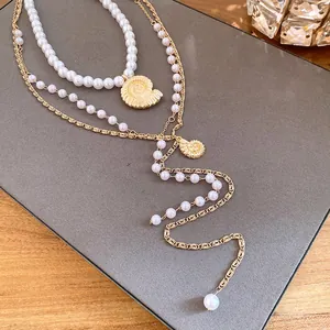 Macro detail showing the layered pearl necklace and gold shell pendant on gray mat