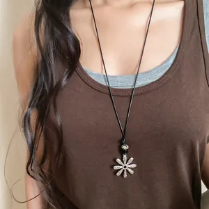 Close-up of a silver flower pendant necklace with a patterned bead on a black cord
