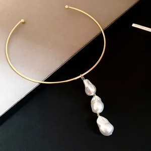 Close-up detail of a minimalist gold metal collar necklace with three baroque pearls.