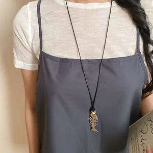 Detailed view of a silver fishbone pendant necklace worn by a model over a grey dress