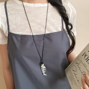 Detailed shot of a silver fishbone pendant necklace on a model wearing grey dress