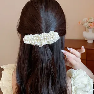 Elegant detail view of a white lace hair clip with pearls on long dark wavy hair