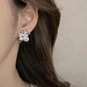 Elegant crystal shell flower earrings with teardrop pearl shown on a model's ear