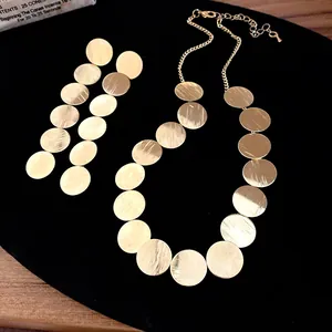 Detailed view of gold circular disk necklace and earrings with brushed metal finish.