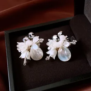 Close-up of white shell flower and crystal teardrop earrings in a velvet jewelry box
