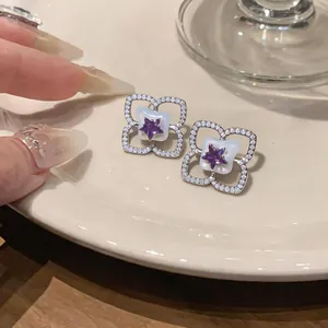Primer plano de pendientes de flor con circonitas y una estrella púrpura central.