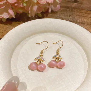 Macro shot of sweet pink cherry earrings with cat-eye stones and zircon leaves