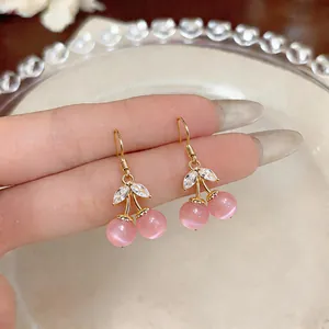 Close-up of sweet pink cat-eye stone cherry earrings with zircon leaves and gold hooks.