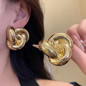 Pendientes de botón dorados con nudo retorcido para mujer lucidos por una modelo.