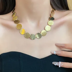 Close-up of a golden circular disc choker necklace featuring a refined brushed metal texture