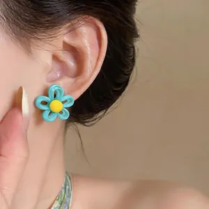 Gros plan détaillé montrant une boucle d'oreille fleur turquoise et jaune portée à l'oreille