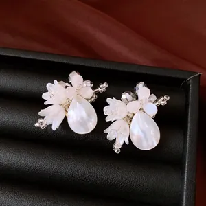Close-up detail shot of elegant floral earrings with shell teardrops and crystal beads.