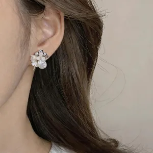 Close-up detail of elegant crystal shell pearl flower teardrop stud earrings worn on ear