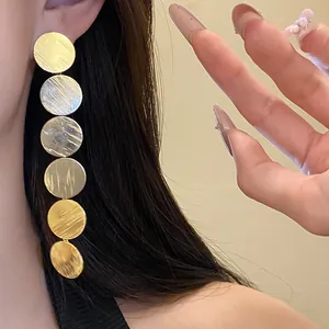 Exquisite detail shot of long brushed gold circular disc earrings worn on a model's ear