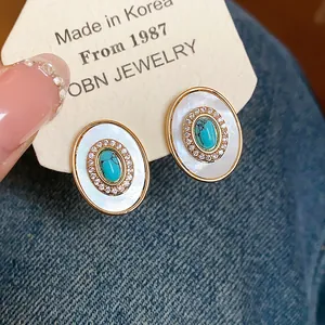Close-up of vintage oval earrings with mother of pearl, turquoise and zircon stones.