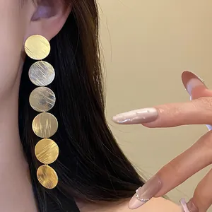 Detailed macro view of long golden dangling earrings featuring six brushed textured circular discs