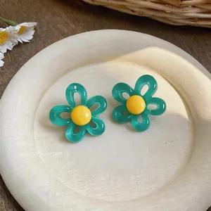 Gros plan sur les boucles d'oreilles fleur dopamine avec contraste turquoise jaune.