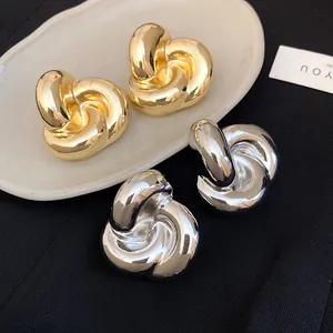 Primer plano de pendientes de flores retorcidas en tonos oro y plata sobre un plato.