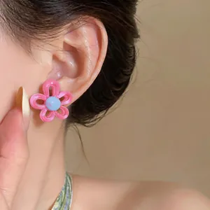 Gros plan détaillé d'une boucle d'oreille fleur rose et bleue portée par un mannequin